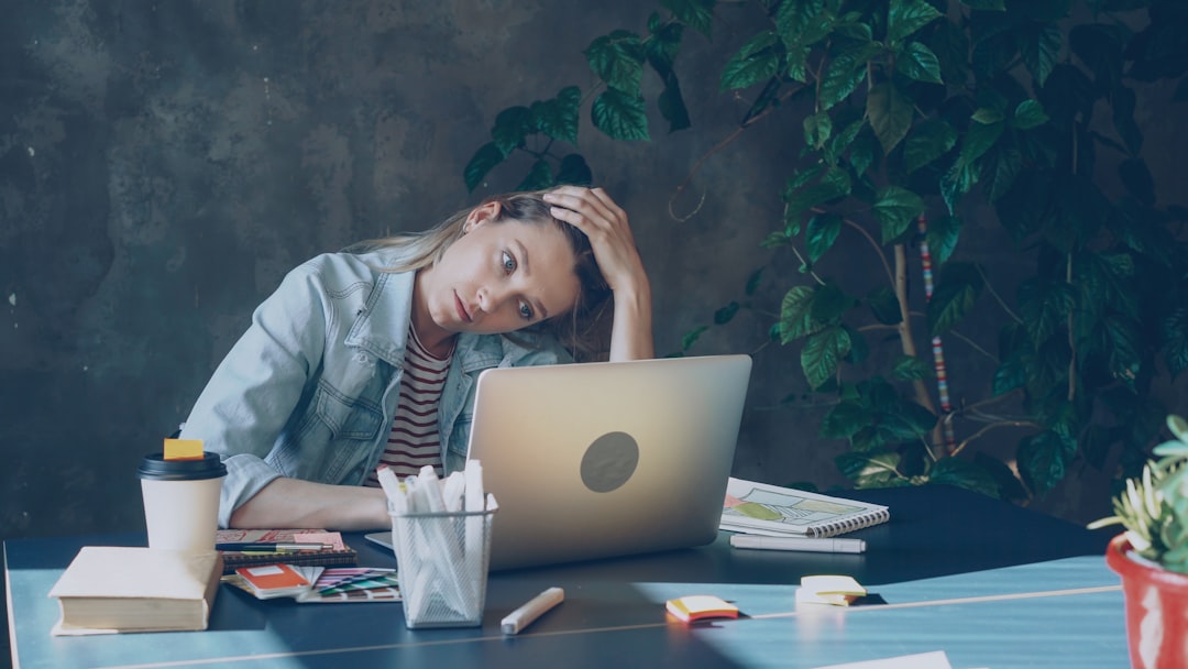 A woman appears stressed while working on laptop. ROI of employee wellbeing extends far beyond reduced absence, it underpins resilience, performance, and competitive advantage.