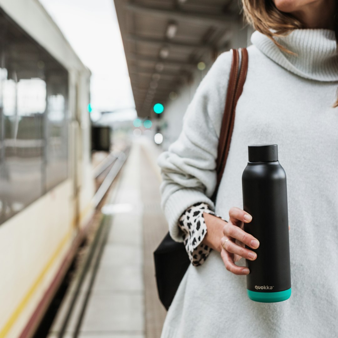 woman in white coat holding black and blue water bottle to aid her hydration habit reboot