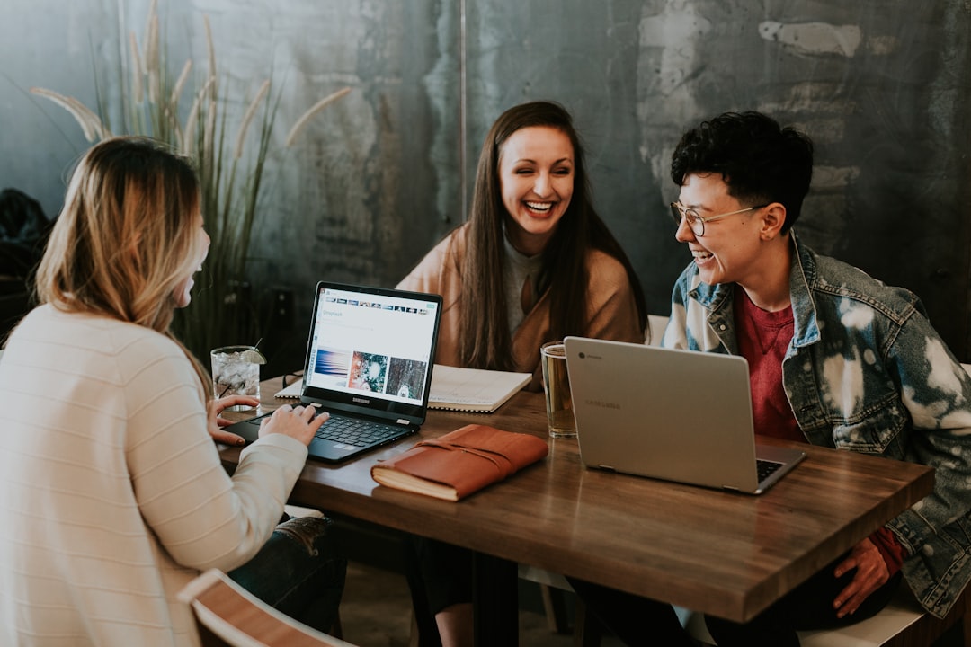 three people sitting in front of table laughing together as they discuss the Key Workplace Wellbeing trend for 2026