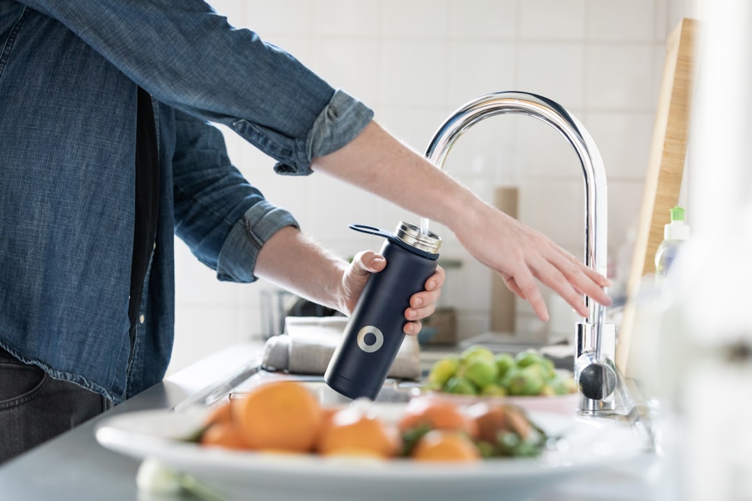 person in blue denim jacket filling up water bottle to stay hydrated
